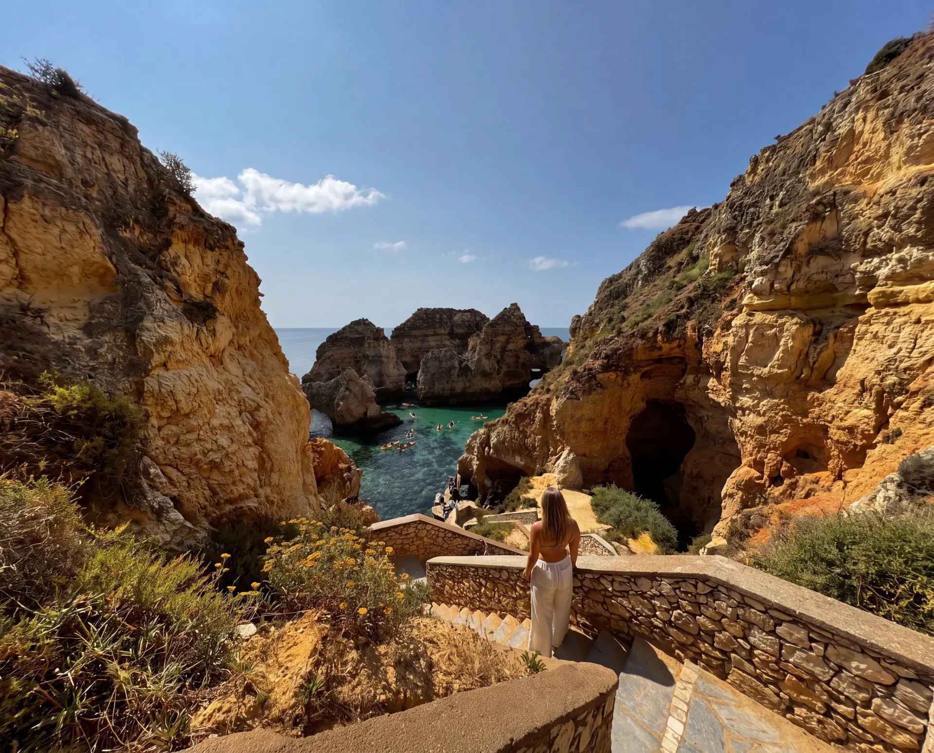 Woman on a stone stairway overlooking turquoise coves and golden cliffs